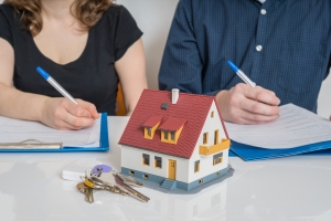 man and woman with pen and paper, model house and keys in front of them representing division of property