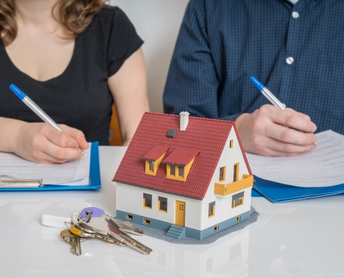 man and woman with pen and paper, model house and keys in front of them representing division of property