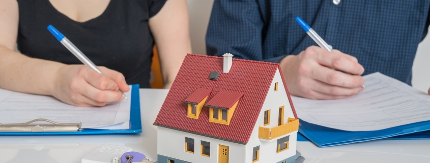 man and woman with pen and paper, model house and keys in front of them representing division of property